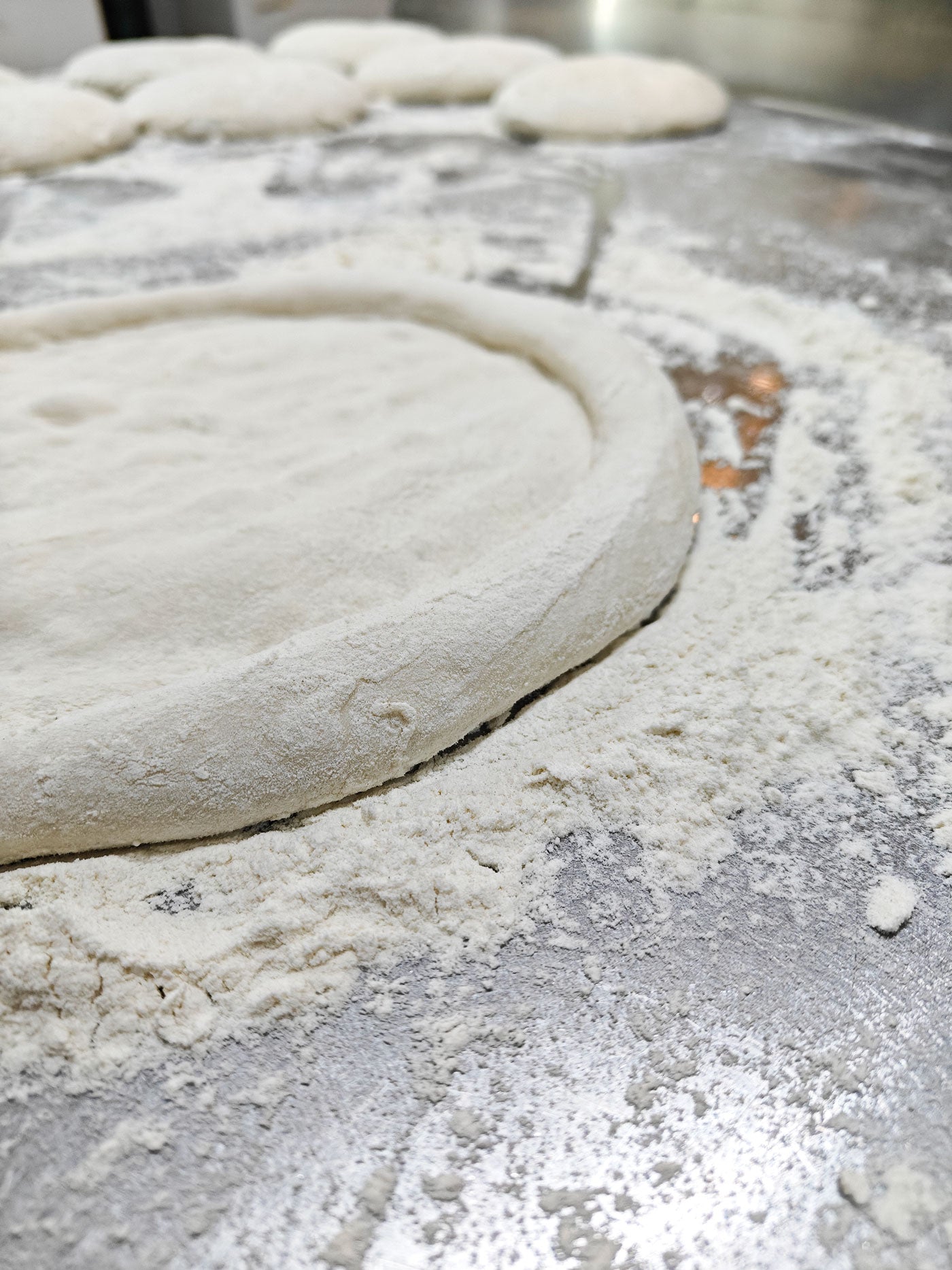 Hand stretched sourdough pizza dough on a floured surface, showcasing the corniccione.